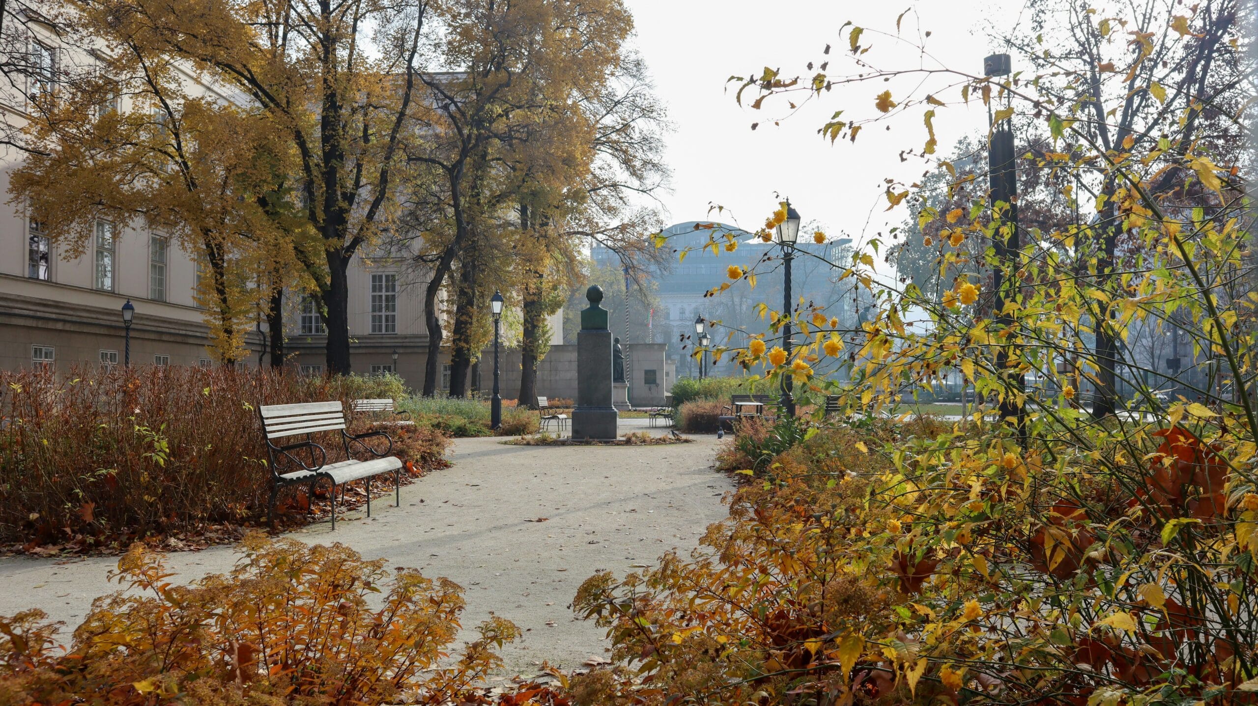 Autumn park in Budapest with benches, yellow trees and statue view