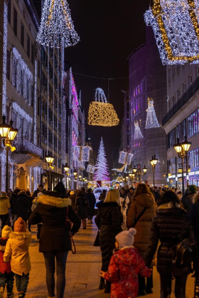 Crowds walking under Christmas lights and decorations on Váci Street in downtown Budapest.