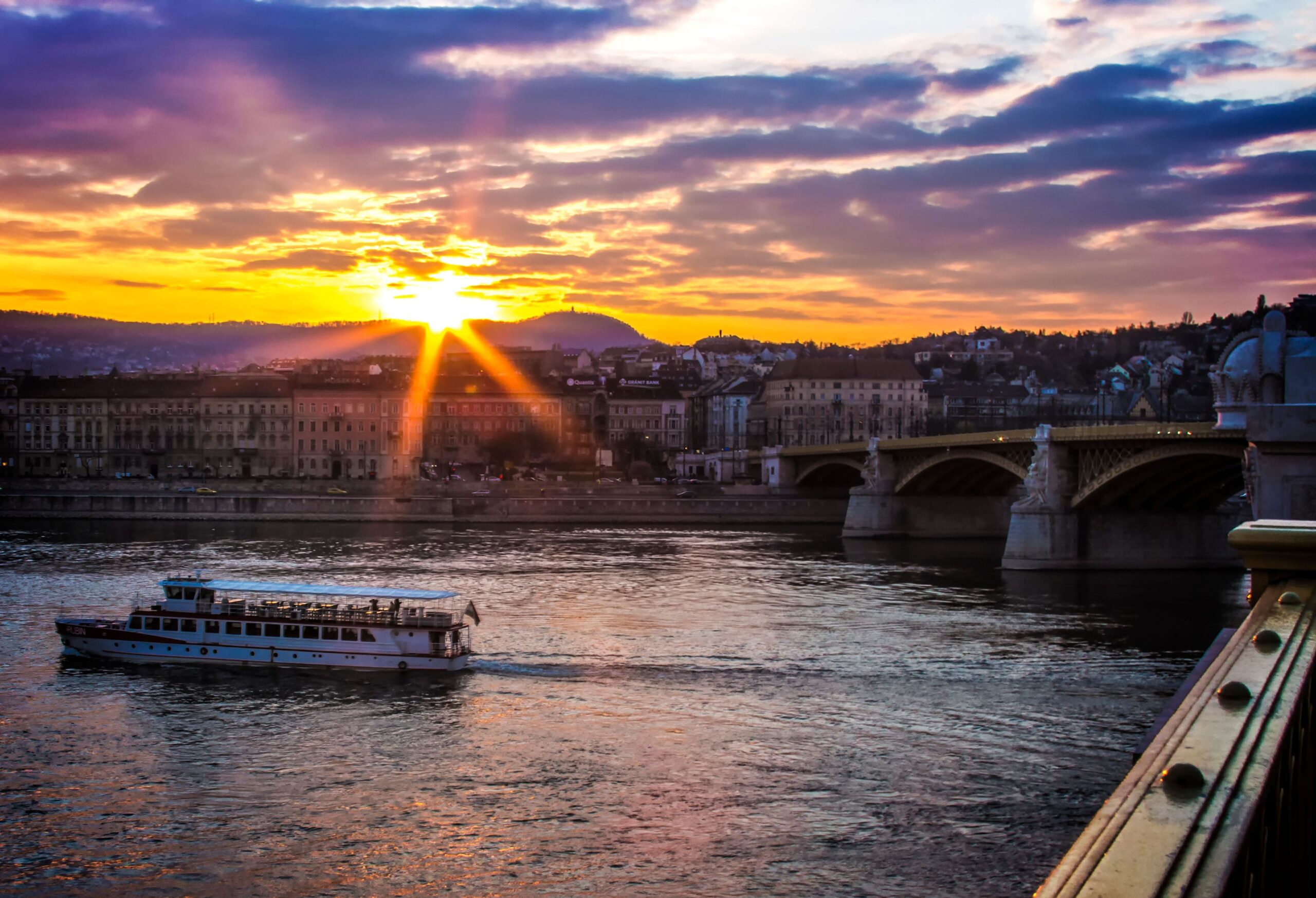 Crucero por el río Danubio al atardecer en Budapest durante el verano con la luz dorada reflejándose sobre el agua y el perfil de la ciudad