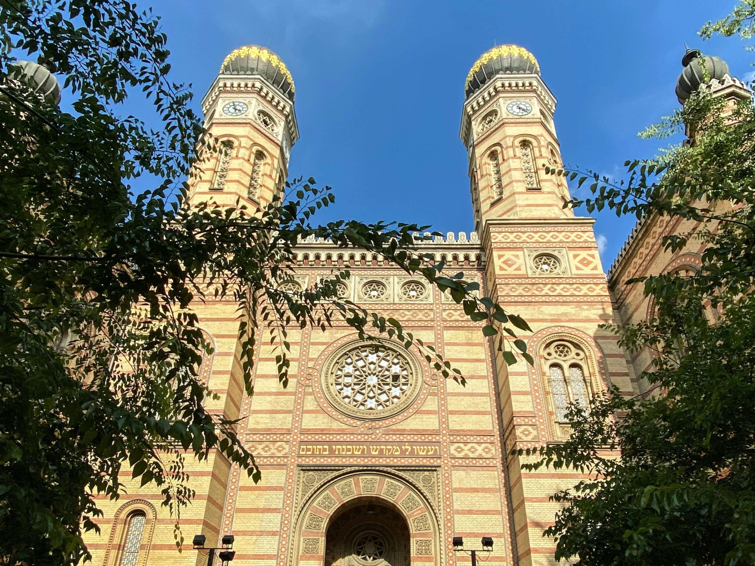 Facade of the Great Synagogue of Budapest on Dohány Street, with twin towers and ornate Moorish Revival architecture under a clear blue sky.