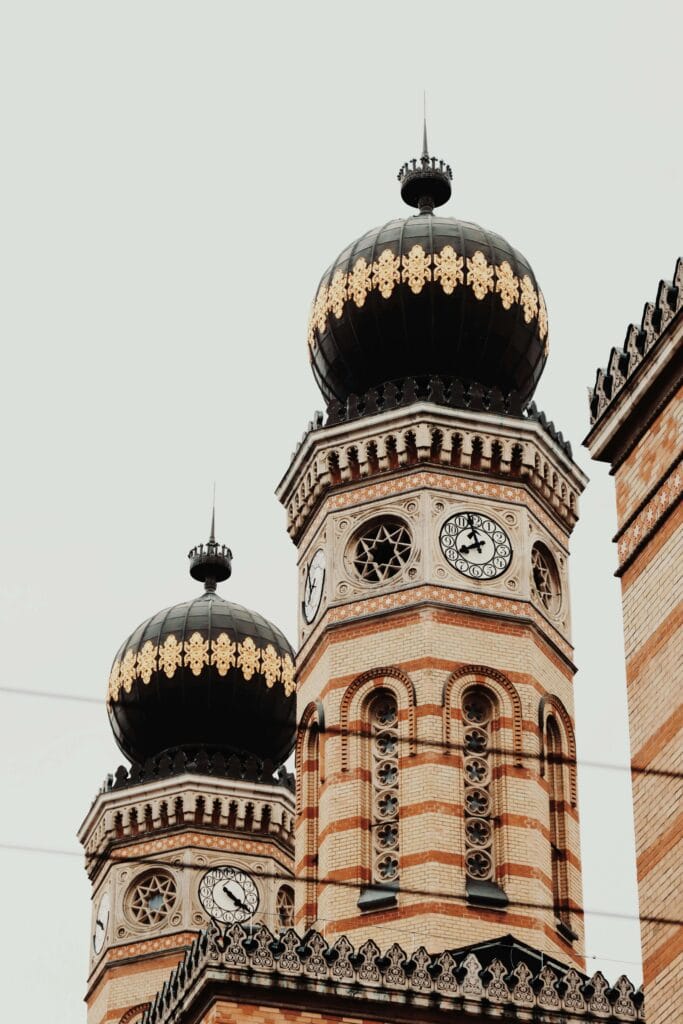 Close-up of the twin towers of the Great Synagogue in Budapest, featuring Moorish Revival design, ornate clocks, and black domes with golden details.