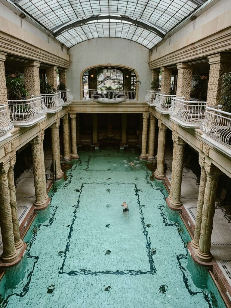 Vista interior de la piscina de estilo Art Nouveau en los Baños Gellért de Budapest, con columnas y luz natural.