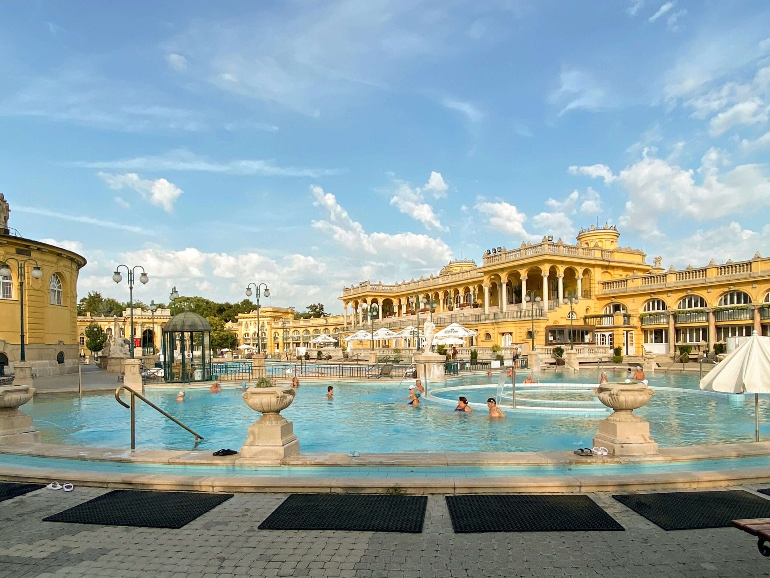 Outdoor pool of Széchenyi Thermal Bath in Budapest on a sunny day, with visitors enjoying the Neo-Baroque architecture.