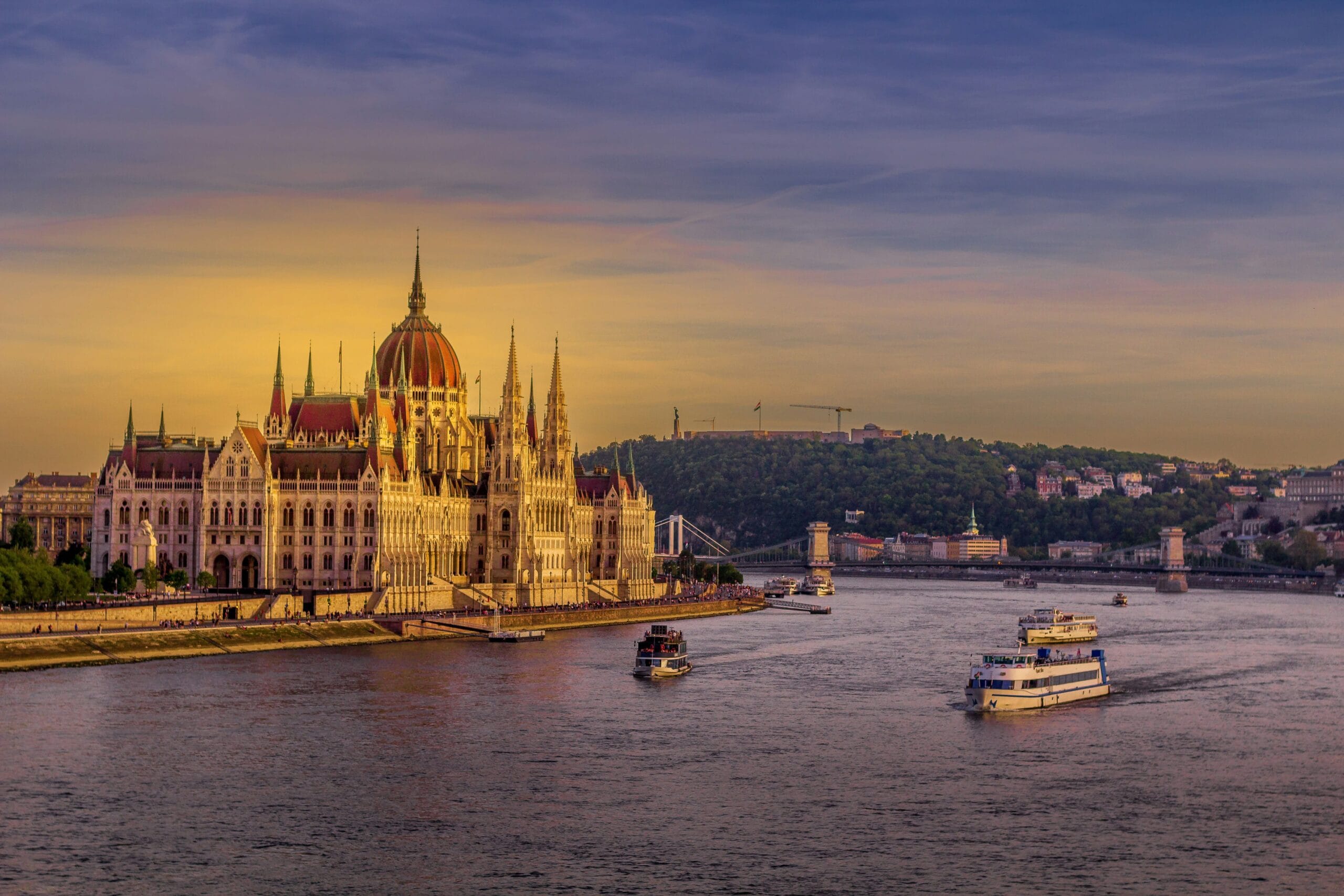Vista al atardecer del Parlamento de Budapest con barcos de crucero navegando por el Danubio.