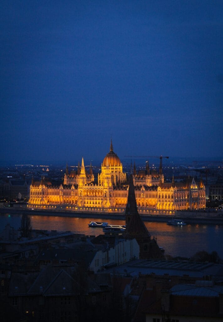 Parlamento de Budapest iluminado de noche con barcos de crucero en el Danubio.