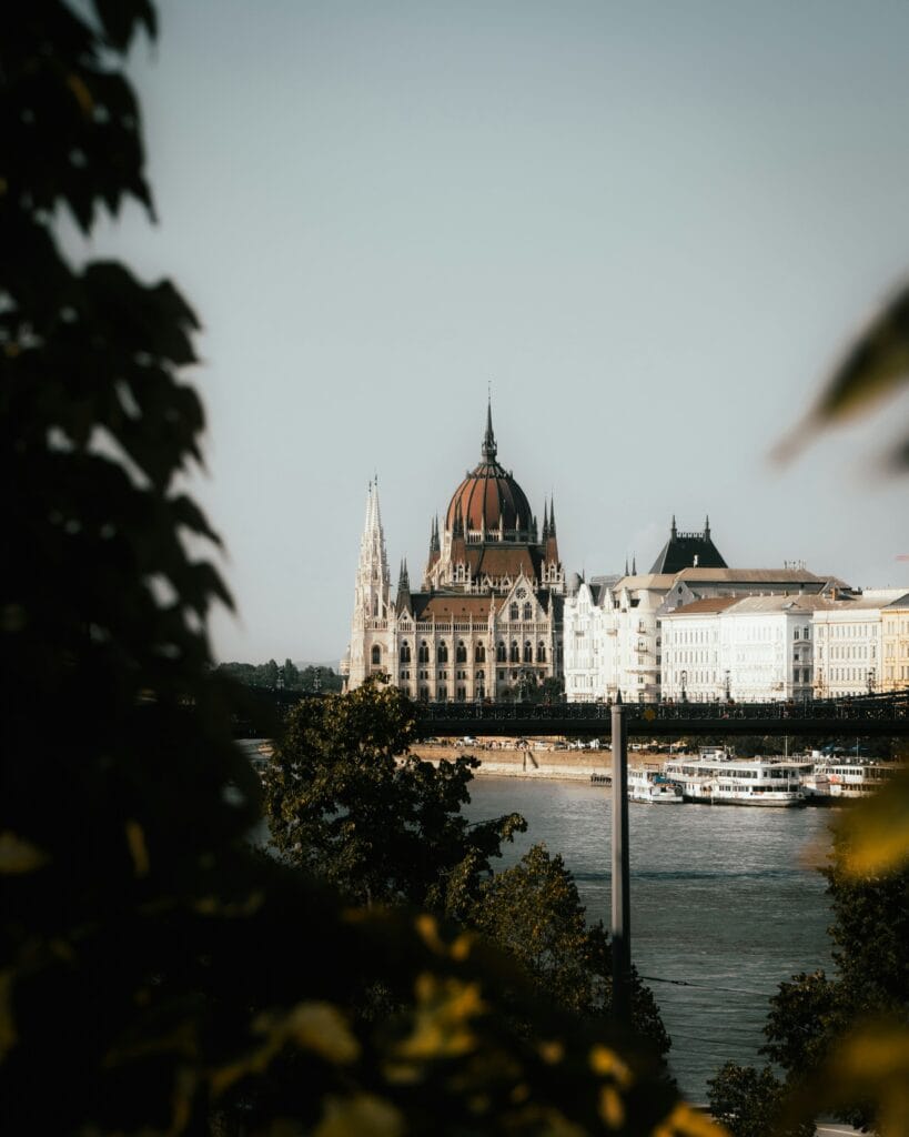 View of the Hungarian Parliament from the Danube, with river cruise boats in daylight.