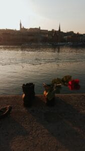 Shoes on the Danube memorial in Budapest at sunset with flowers and Buda Castle in the background